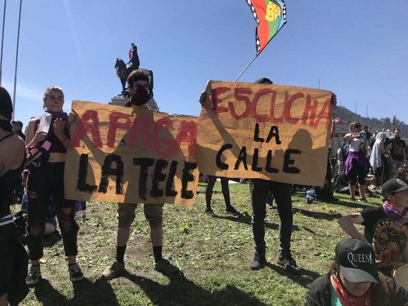 Manifestantes en Plaza Dignidad con carteles "Apaga la tele" y "Escucha la calle"